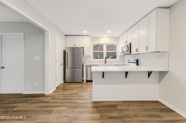 kitchen featuring kitchen peninsula, white cabinets, appliances with stainless steel finishes, a kitchen breakfast bar, and hardwood / wood-style flooring