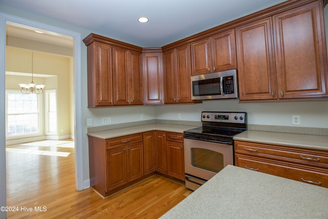 kitchen with light hardwood / wood-style flooring, stainless steel appliances, an inviting chandelier, and hanging light fixtures