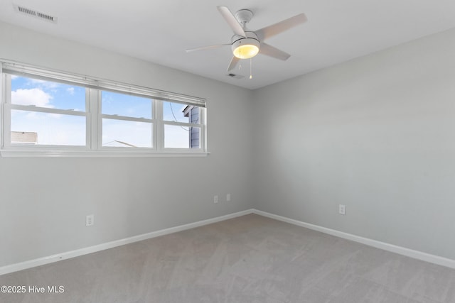 spare room with a ceiling fan, light colored carpet, visible vents, and baseboards