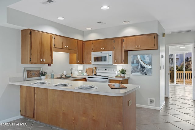 kitchen with light tile patterned floors, visible vents, light countertops, white appliances, and a peninsula