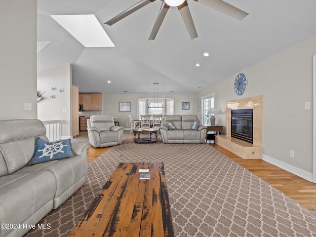 living room featuring a premium fireplace, light hardwood / wood-style flooring, ceiling fan, and lofted ceiling with skylight