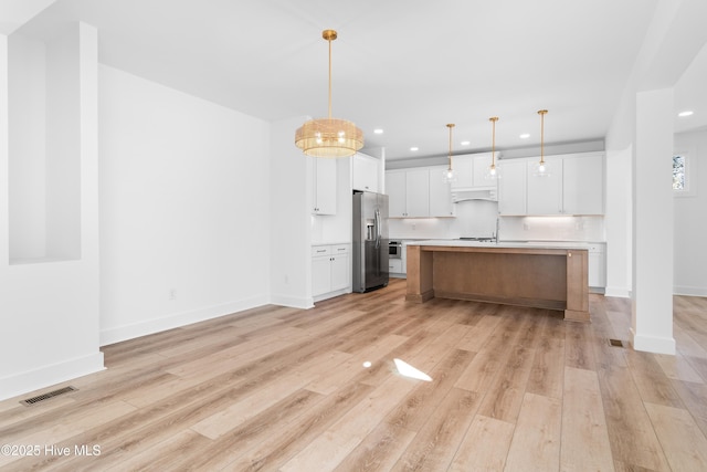 kitchen featuring hanging light fixtures, stainless steel fridge with ice dispenser, custom range hood, a kitchen island with sink, and white cabinets