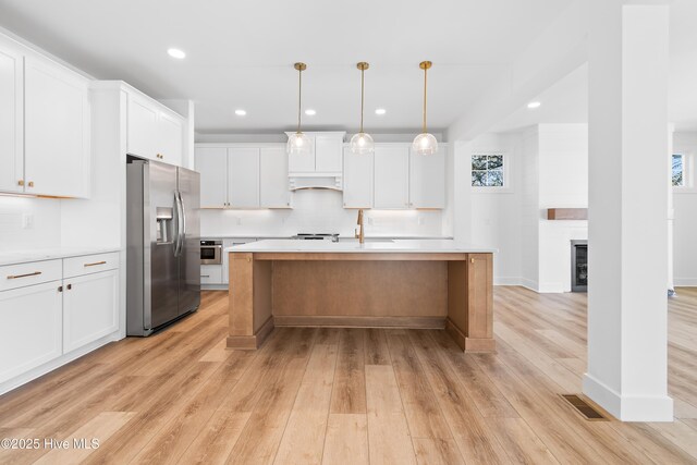 kitchen with a large fireplace, decorative light fixtures, stainless steel appliances, a kitchen island with sink, and white cabinets