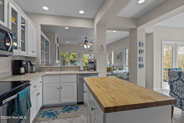 kitchen with stainless steel appliances, butcher block counters, white cabinetry, kitchen peninsula, and ceiling fan