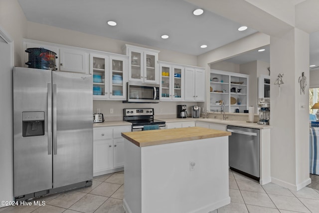 kitchen featuring stainless steel appliances, light tile patterned flooring, white cabinets, and a kitchen island