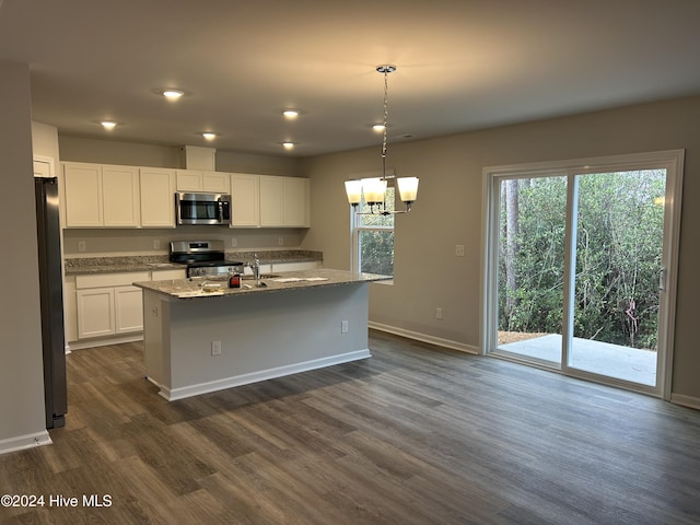 kitchen featuring light stone countertops, white cabinets, decorative light fixtures, stainless steel appliances, and an island with sink