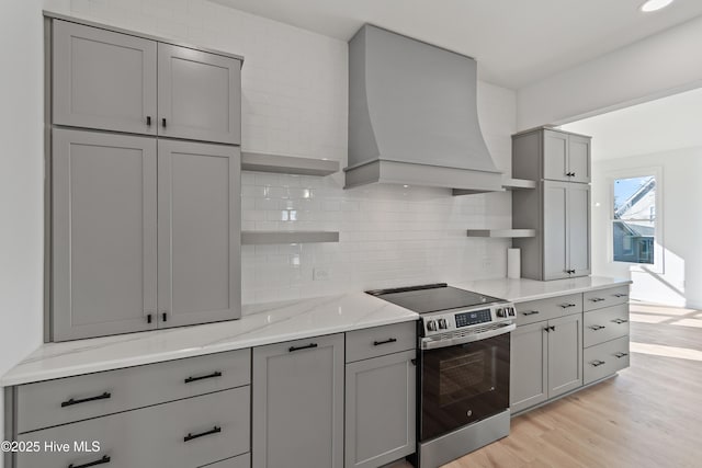 kitchen with electric range, custom exhaust hood, gray cabinetry, decorative backsplash, and light hardwood / wood-style flooring