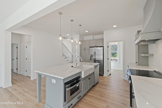 kitchen with custom exhaust hood, a center island with sink, gray cabinets, appliances with stainless steel finishes, and sink