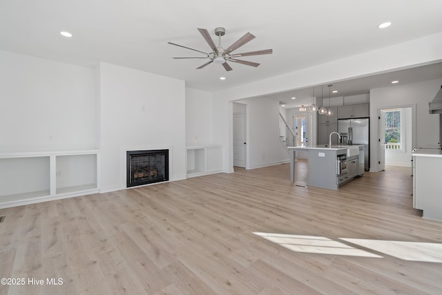 unfurnished living room featuring a fireplace, built in features, ceiling fan, and light hardwood / wood-style floors