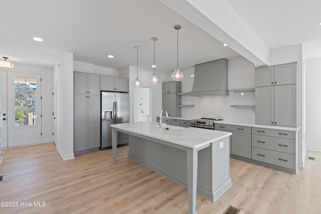 kitchen featuring a kitchen island with sink, appliances with stainless steel finishes, custom range hood, pendant lighting, and tasteful backsplash