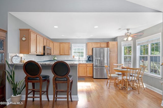 kitchen with kitchen peninsula, backsplash, appliances with stainless steel finishes, light stone countertops, and light hardwood / wood-style flooring
