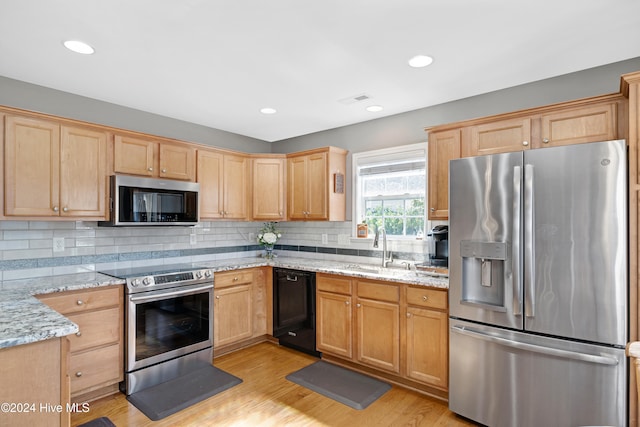 kitchen with appliances with stainless steel finishes, light stone countertops, sink, and light wood-type flooring