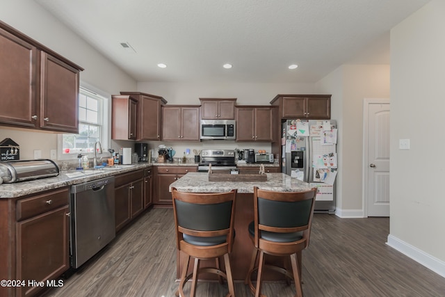 kitchen featuring stainless steel appliances, sink, a breakfast bar, dark wood-type flooring, and a center island