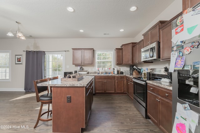 kitchen with an island with sink, dark hardwood / wood-style flooring, a kitchen breakfast bar, and appliances with stainless steel finishes