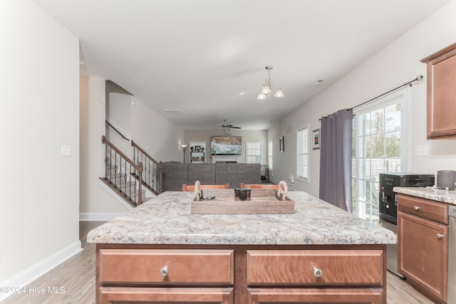 kitchen with a center island with sink, light hardwood / wood-style flooring, light stone countertops, dishwasher, and ceiling fan with notable chandelier