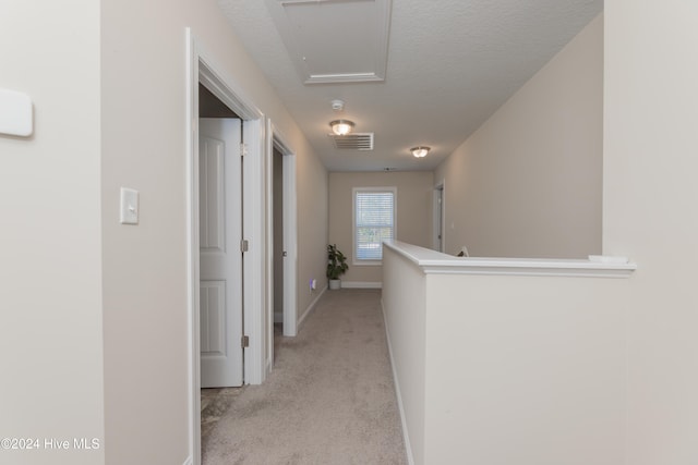 hallway with a textured ceiling and light carpet