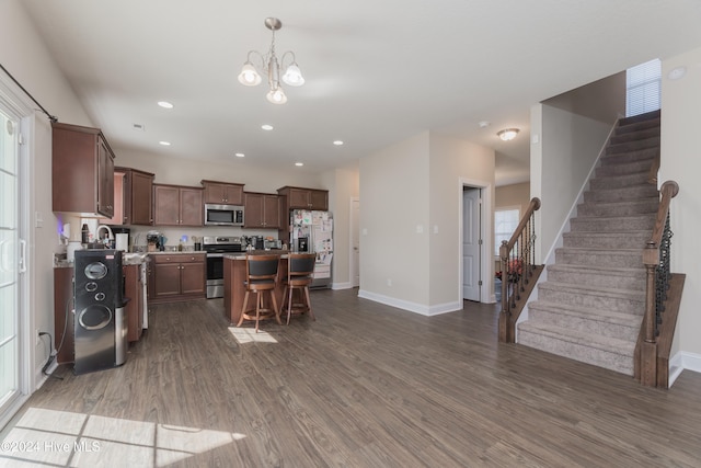 kitchen with stainless steel appliances, a breakfast bar area, a chandelier, a kitchen island, and dark hardwood / wood-style flooring