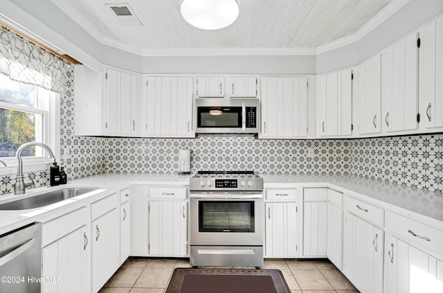 kitchen with appliances with stainless steel finishes, ornamental molding, sink, light tile patterned floors, and white cabinets