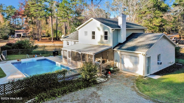 rear view of property featuring a fenced in pool, a sunroom, and a garage