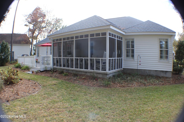 rear view of property featuring a lawn, a sunroom, and a deck