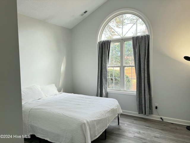 bedroom featuring hardwood / wood-style floors, lofted ceiling, and a textured ceiling