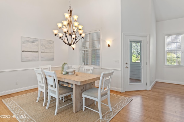 dining room featuring a chandelier, a towering ceiling, light wood-style flooring, and baseboards