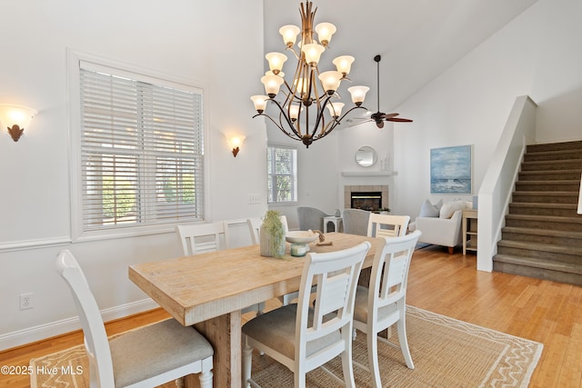 dining space with baseboards, a tile fireplace, stairs, light wood-type flooring, and high vaulted ceiling