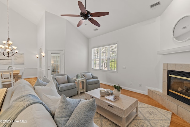 living area featuring high vaulted ceiling, a tile fireplace, visible vents, baseboards, and light wood finished floors