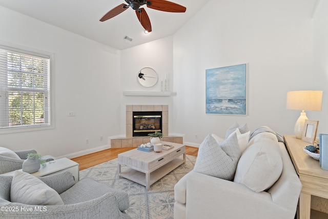 living room featuring baseboards, visible vents, a tiled fireplace, wood finished floors, and vaulted ceiling