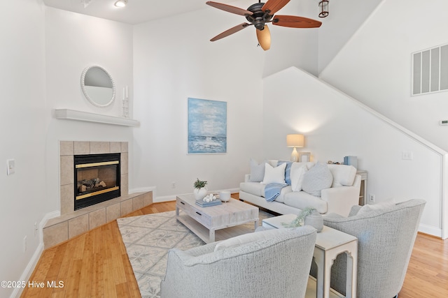 living room with wood finished floors, visible vents, baseboards, a ceiling fan, and a tiled fireplace