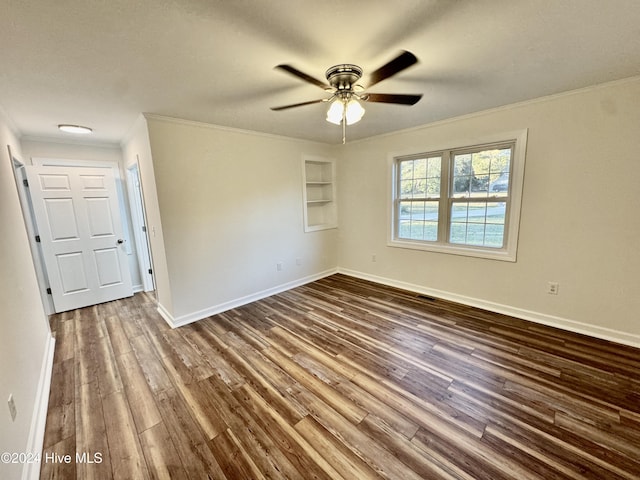 empty room featuring built in shelves, ceiling fan, crown molding, and dark hardwood / wood-style floors