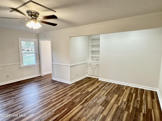 unfurnished room with dark wood-type flooring, built in features, ceiling fan, and ornamental molding