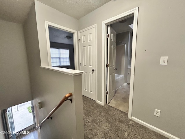 hall featuring a textured ceiling and dark carpet