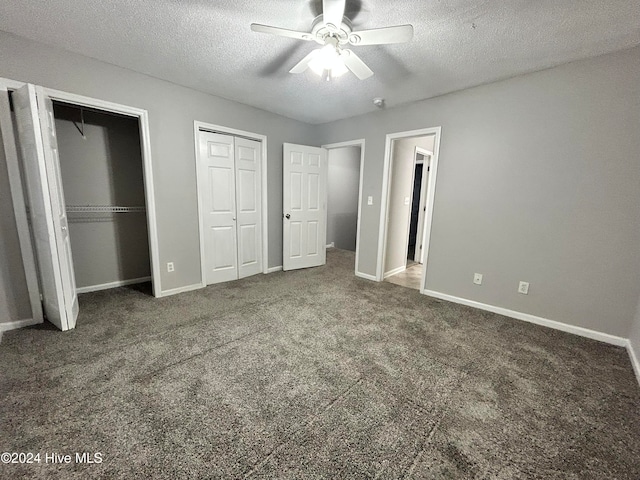 unfurnished bedroom with multiple closets, dark colored carpet, a textured ceiling, and ceiling fan