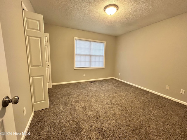 empty room featuring a textured ceiling and dark carpet