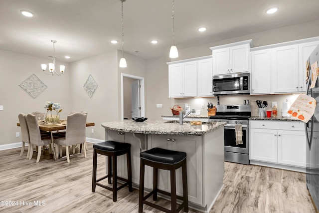 kitchen featuring a center island with sink, white cabinetry, decorative light fixtures, and stainless steel appliances