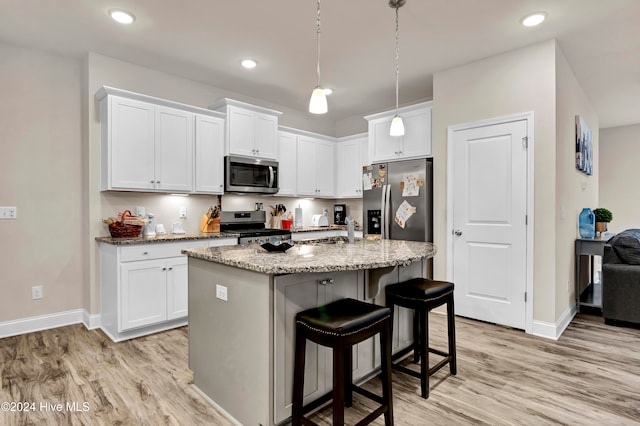 kitchen with an island with sink, stainless steel appliances, light stone countertops, light wood-type flooring, and white cabinetry