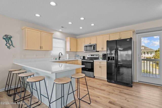 kitchen with appliances with stainless steel finishes, sink, light wood-type flooring, kitchen peninsula, and a kitchen breakfast bar