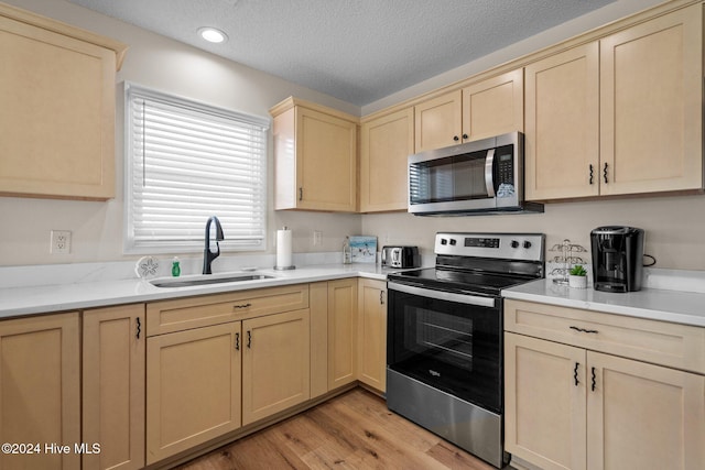 kitchen with appliances with stainless steel finishes, sink, a textured ceiling, light hardwood / wood-style flooring, and light brown cabinets