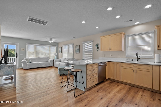 kitchen with a breakfast bar area, kitchen peninsula, sink, light wood-type flooring, and a textured ceiling