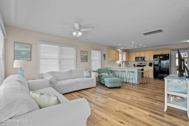 living room with sink, ceiling fan, light hardwood / wood-style floors, and plenty of natural light