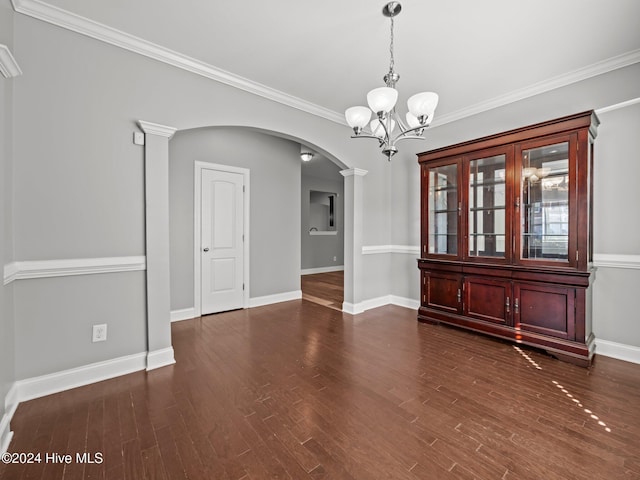 unfurnished dining area featuring dark wood-style floors, an inviting chandelier, arched walkways, and ornate columns