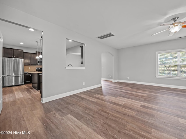 unfurnished living room featuring baseboards, ceiling fan, visible vents, wood finished floors, and arched walkways