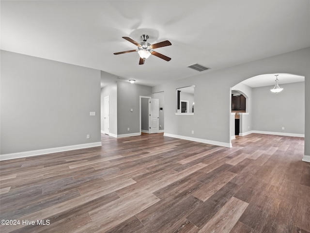 unfurnished living room with a ceiling fan, baseboards, visible vents, wood finished floors, and arched walkways