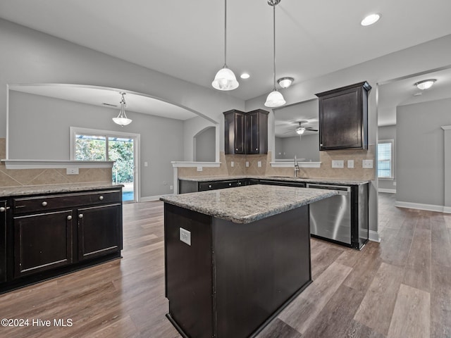 kitchen featuring a center island, arched walkways, dishwasher, a sink, and backsplash