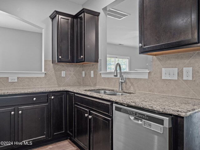 kitchen with a sink, stainless steel dishwasher, tasteful backsplash, and light stone counters