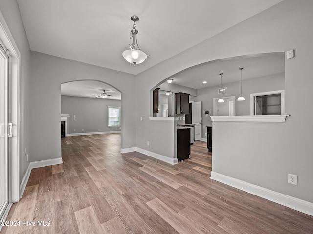 unfurnished living room with wood finished floors, a fireplace, ceiling fan, arched walkways, and baseboards