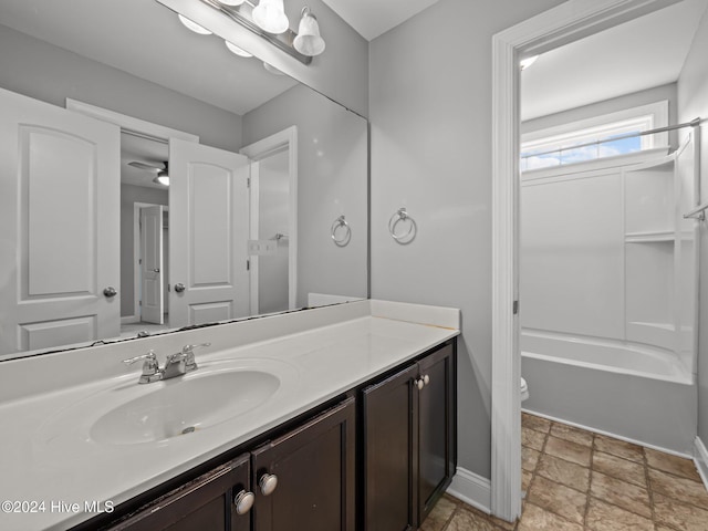 bathroom featuring toilet, vanity, stone finish floor, washtub / shower combination, and baseboards