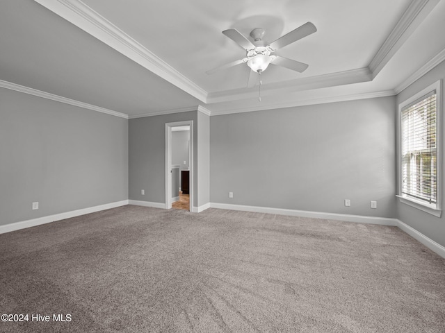 spare room with a tray ceiling, carpet floors, crown molding, baseboards, and ceiling fan