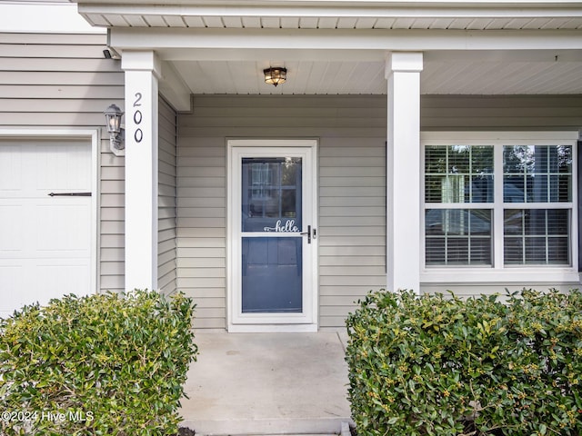 view of exterior entry with a garage and a porch